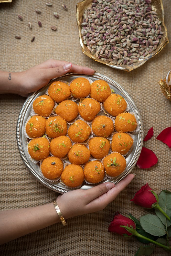 Top view of hands holding a tray of Indian laddus with festive decorations.